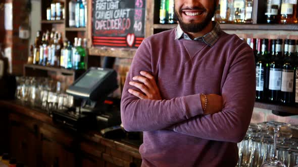 Portrait of barman standing with arms crossed at bar counter