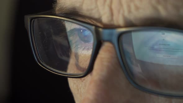 Closeup of a Focused Mature Man with Glasses and a Laptop Working on the Internet Until Late at