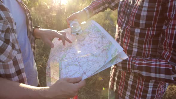 Travelers with a map and a compass in their hands are looking for their way. Terrain orientation.