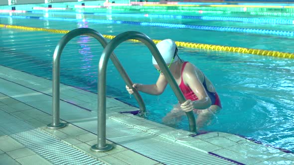 Side View Young Woman Swimmer Comes Out of Indoor Swimming Pool with Blue Water, Slow Motion,