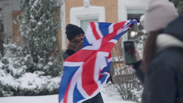 Joyful African American Man Having Fun Posing with British Flag on Winter Backyard As Teen Girl