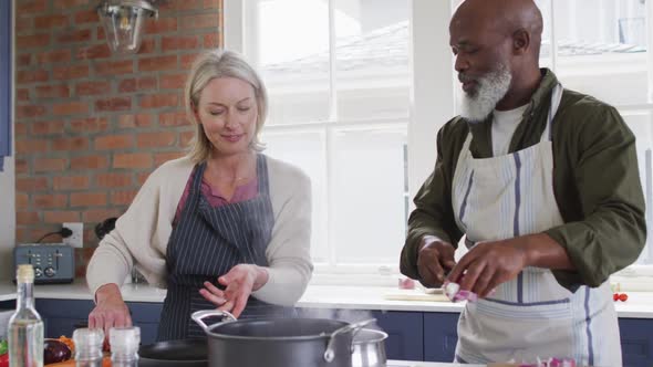 Mixed race couple wearing aprons cooking together in the kitchen at home