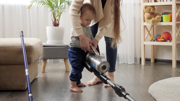 Mother doing housework teaching and giving vacuum cleaner to her baby