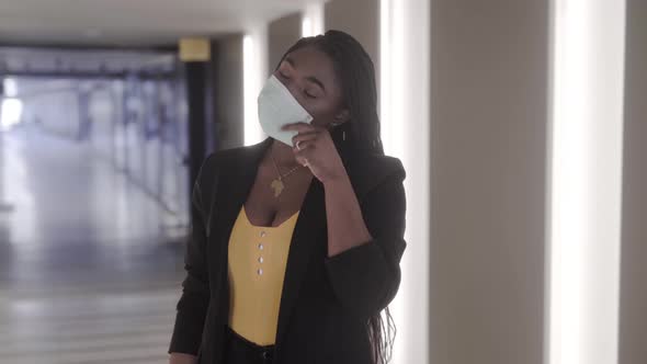Smiling black woman taking off sterile mask in building corridor