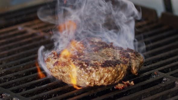 Slow motion of beef hamburger on a grill in close up with flames and smoke