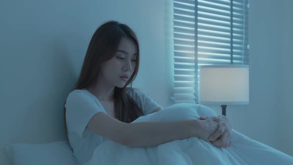 Attractive unhappy depressed young woman feel sad and upset with life problem sit on bed at night.