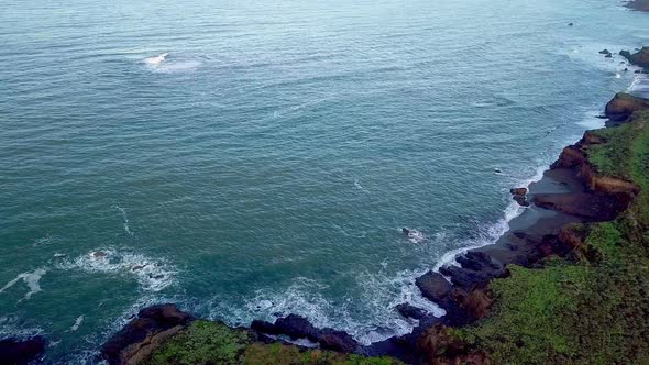 Rising aerial view of waves crashing on beach cliffs on California coast