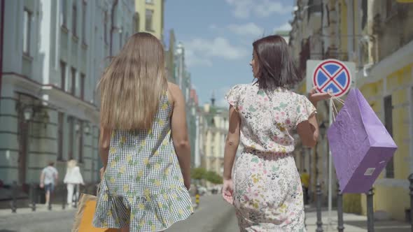 Two Cheerful Women with Shopping Bags Walking Through City Street