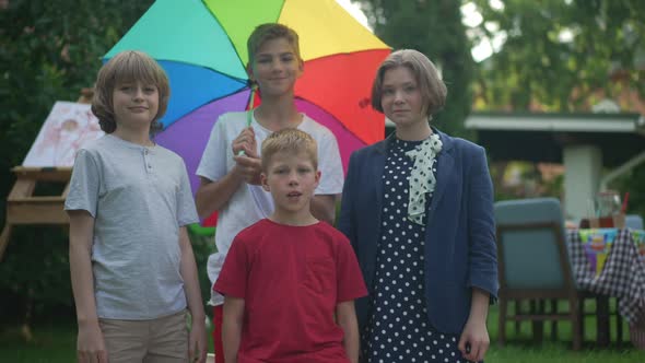 Medium Shot Positive Caucasian Boys and Girl Looking at Camera Smiling Spinning Colorful Umbrella