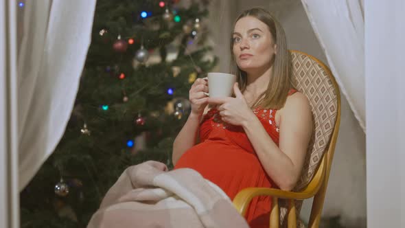 Side View Portrait of Relaxed Smiling Pregnant Woman Drinking Tea Sitting on Rocking Chair on