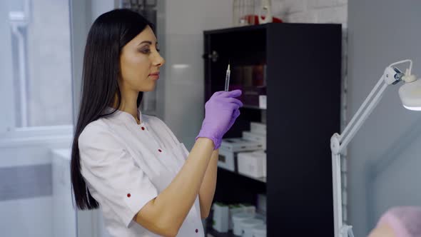 Cute Cosmetologist with Long Hair Checks a Syringe Before the Botox Procedure 