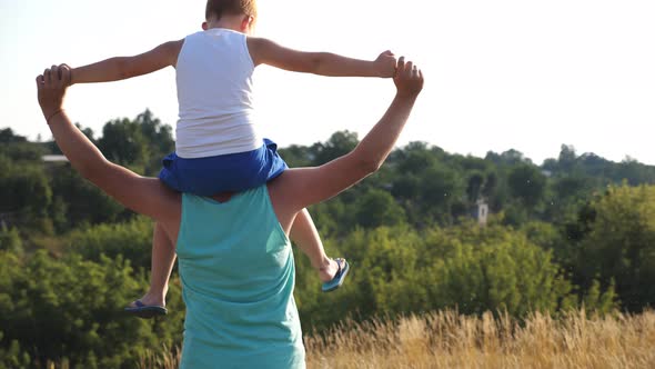 Cheerful Father Holding His Smiling Son on Shoulders and Spinning Around at Meadow on Sunny Summer