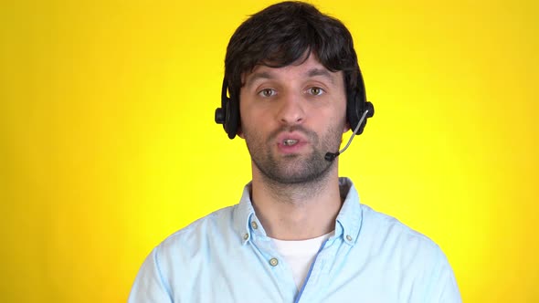 Successful Man in Headset Gesturing and Talking on Camera on a Yellow Background