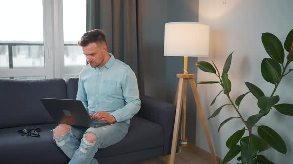 Man with Glasses Sitting on the Sofa with Laptop and Working in Cozy Room