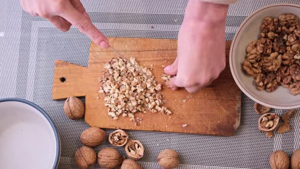 Chopping Walnuts Cores with Kitchen Knife on a Wood Cutting Board