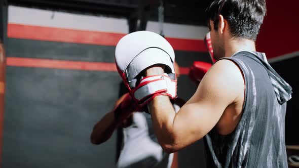 boxer is practicing punching sandbags and battling with a trainer inside the gym