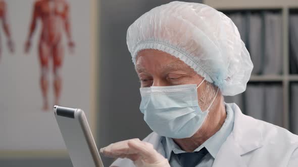 Elderly Doctor in Protective Clothes Using Tablet in Hospital