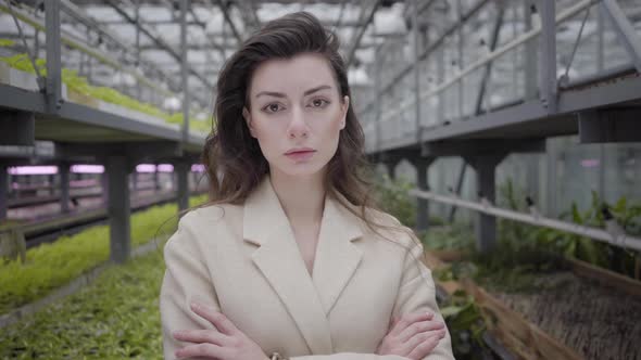 Beautiful Caucasian Woman Standing in Glasshouse with Hands Crossed. Camera Approaching To Face of