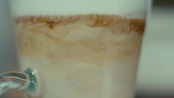 Coffee latte in glass layers mix up with spoon close up