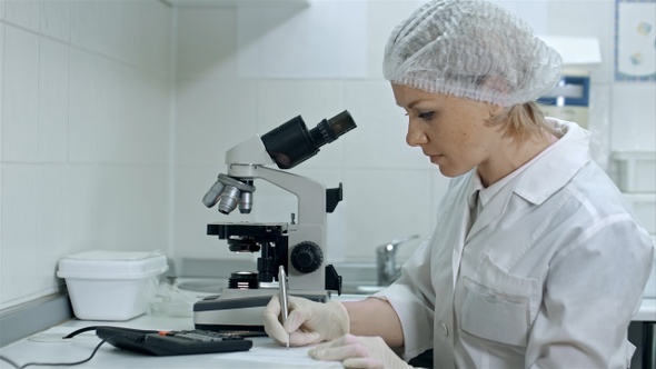 Scientist Working with Microscope Calculating and Taking