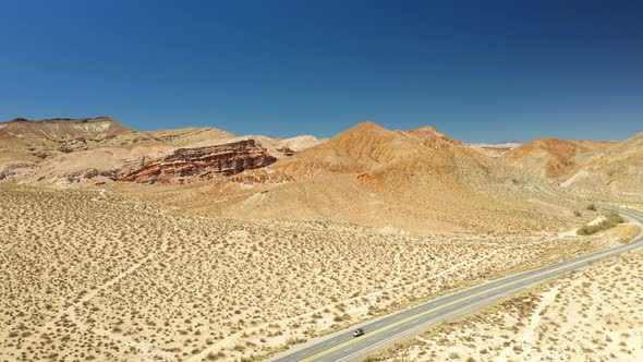 A lonely highway through the rugged and arid landscape of the Mojave Desert - descending aerial view