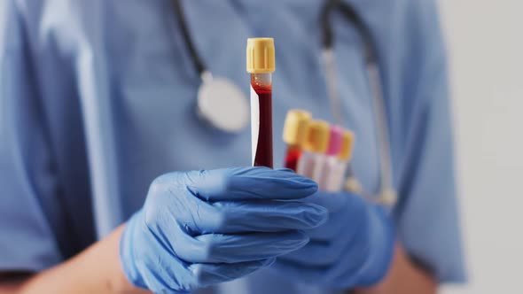 Video of biracial female doctor holding test tubes on blue background