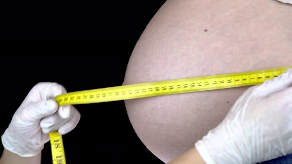 The Doctor Measures the Size of the Belly of a Pregnant Woman. Young Woman with a Big Belly