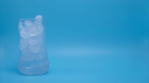 Time-lapse video, the ice in clear glass melting on blue background.