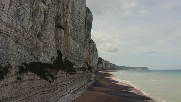 The Drone Flies at the Foot of Sheer Striped Cliffs with a Pebbly Shore