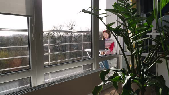 Pretty Teenager Girl Is Typing, Working on Laptop, on Open Balcony. Spring Sunny Day. Concept of