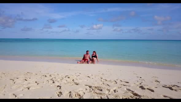 Family of two tanning on beautiful coastline beach time by aqua blue sea with bright sand background