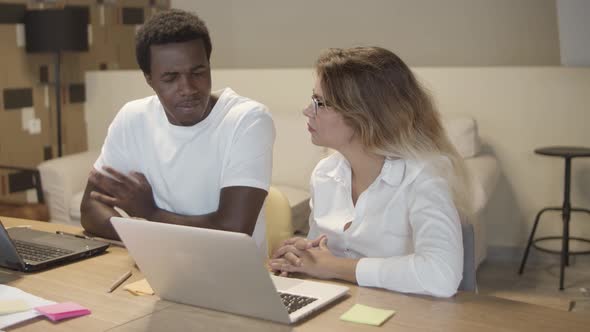 Diverse Couple of Colleagues Sitting at Table with Laptops