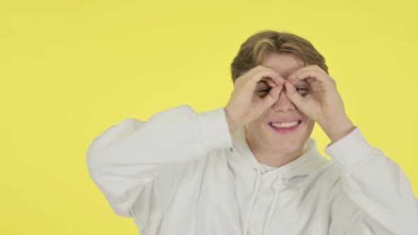 Young Man Searching with Handmade Binocular on Yellow Screen