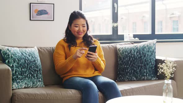 Smiling Asian Woman with Smartphone at Home