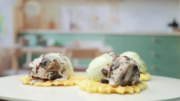 Melting Pistachio and Chocolate Ice Ream Balls on the Top of Waffles Rotating in the Kitchen in Slow