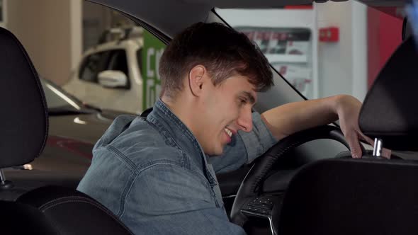 Happy Handsome Man Showing Thumbs Up, Sitting in a New Car at the Dealership