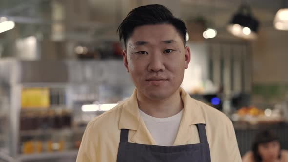 Portrait of Friendly Asian Waiter in Apron Posing at Cafe