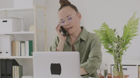 Young Female Between 30 and 40 Years Old is Speaking on Phone in Front of Pc