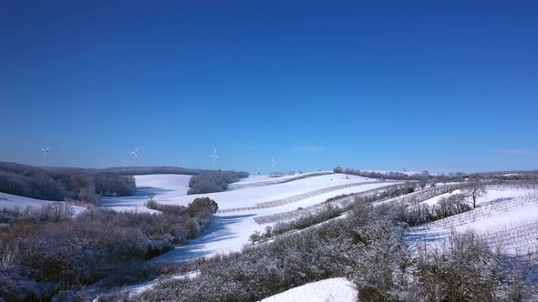 Drone Flight Over Snow-covered Agricultural Landscape On Sunny Day In Winter With Wind Turbines In D