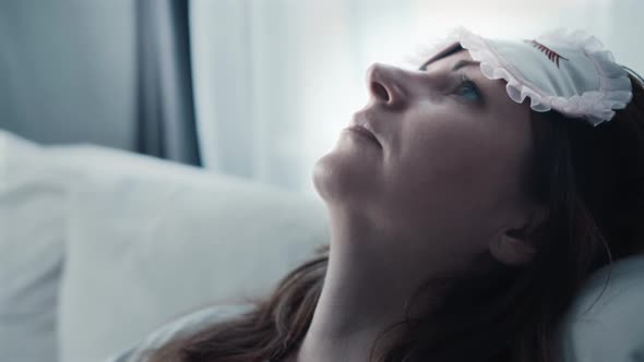 Sad Tired Woman Puts Her Head on the Back of the Sofa and Pulls a Sleep Mask Over His Eyes