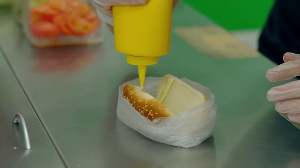 CU, Slow Motion: Cook Prepares a Hot Dog, Pours Mayonnaise on a Roll.