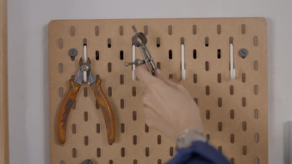 A Hand Of An Artisan Jeweler Getting A Plier And Adjuster Tools On Wall Hooks Static