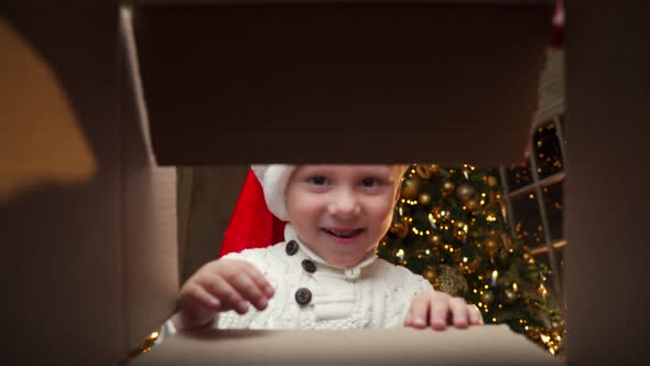 Happy Boy in a Santa Claus Hat Looks Into the Box Smiles and Holds Out His Hands