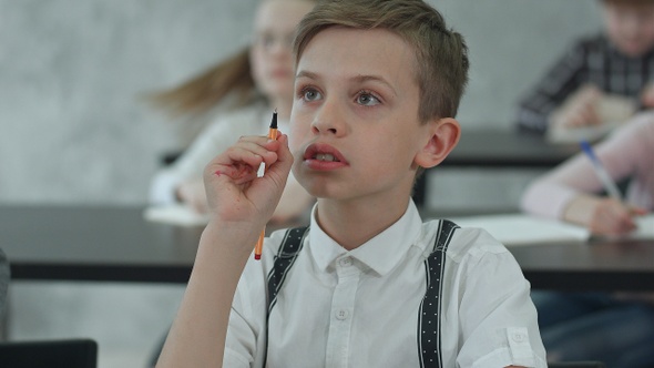 Little boy sitting at table and listening in class