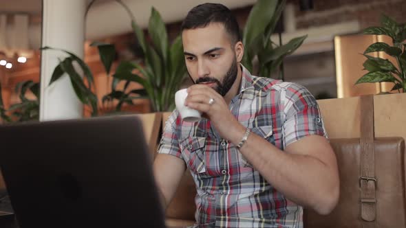 Man Drinking Coffee and Working on Laptop