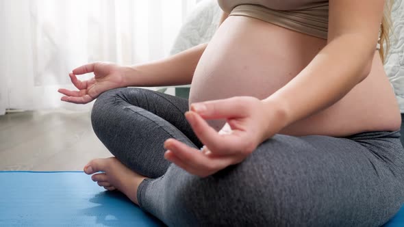 CLoseup of Pregnant Woman Folding Her Fingers and Sitting in Lotus Yoga Pose on Fitness Mat at Big