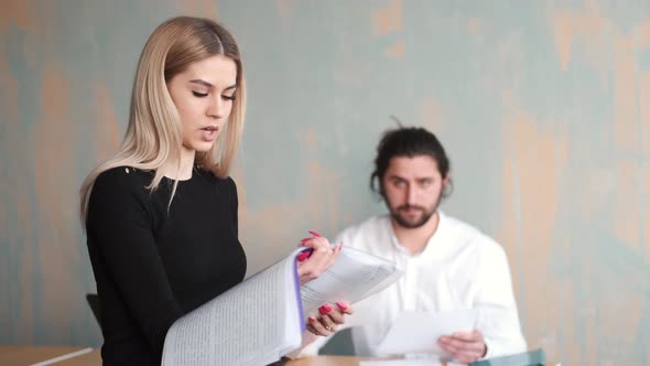 Young Woman Office Worker Close Up Work with Papers and Her Male Collegue at the Background