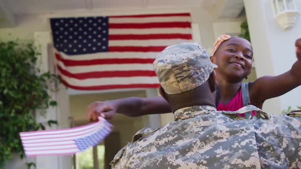 African american soldier father hugging smiling daughter in front of house with american flag