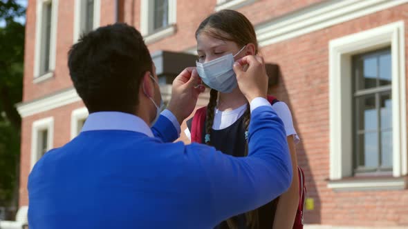 Dad Putting Protective Mask on Daughter Face Outside School Building