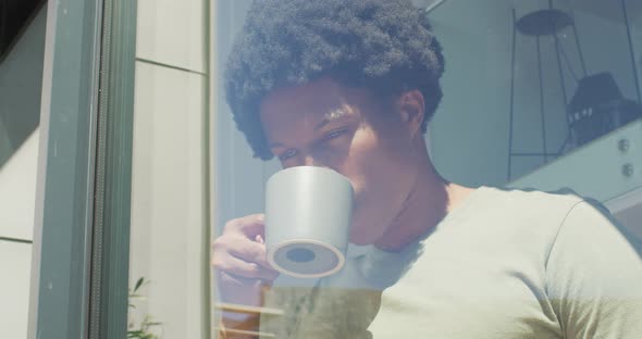 African american man looking at the window and drinking coffee at home